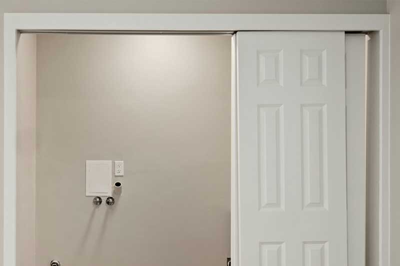 Empty laundry closet with white sliding doors, hookups for washer and dryer visible on the back wall.