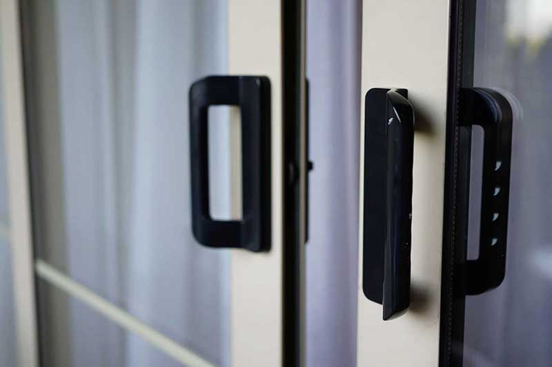 Close-up of black handles on a glass sliding door with white curtains in the background.