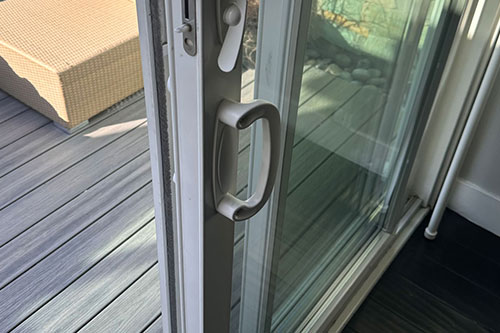 Partially open sliding glass door with metal handle, leading out to a deck with a wicker chair.