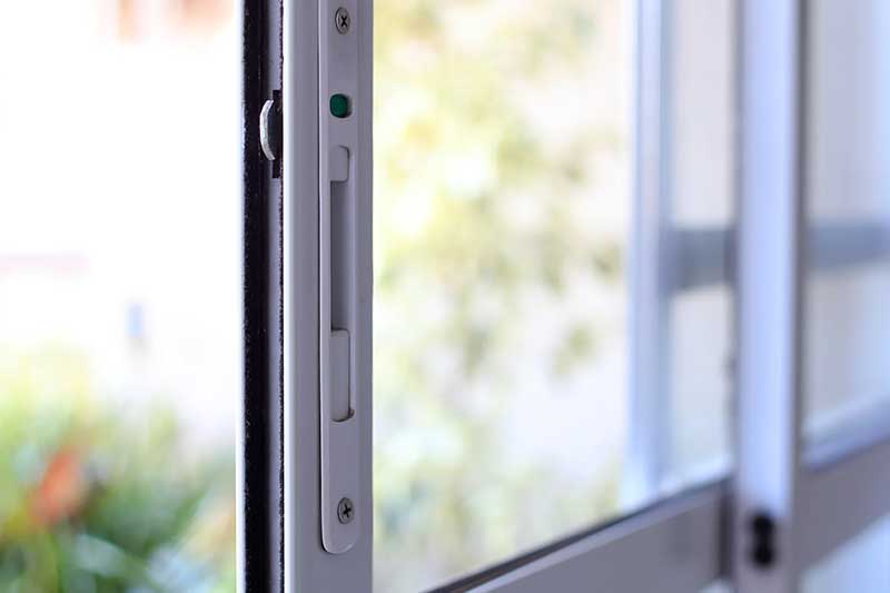 Close-up of a sliding glass door lock, with the door partially open and a blurred outdoor background.
