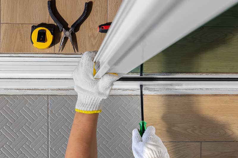 Person wearing gloves using a screwdriver to fix a sliding door, with tools laid out on the floor nearby.