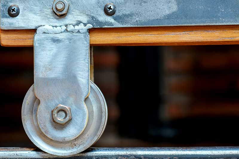 Close-up of a metal wheel with bolts attached to a sliding mechanism on a track.