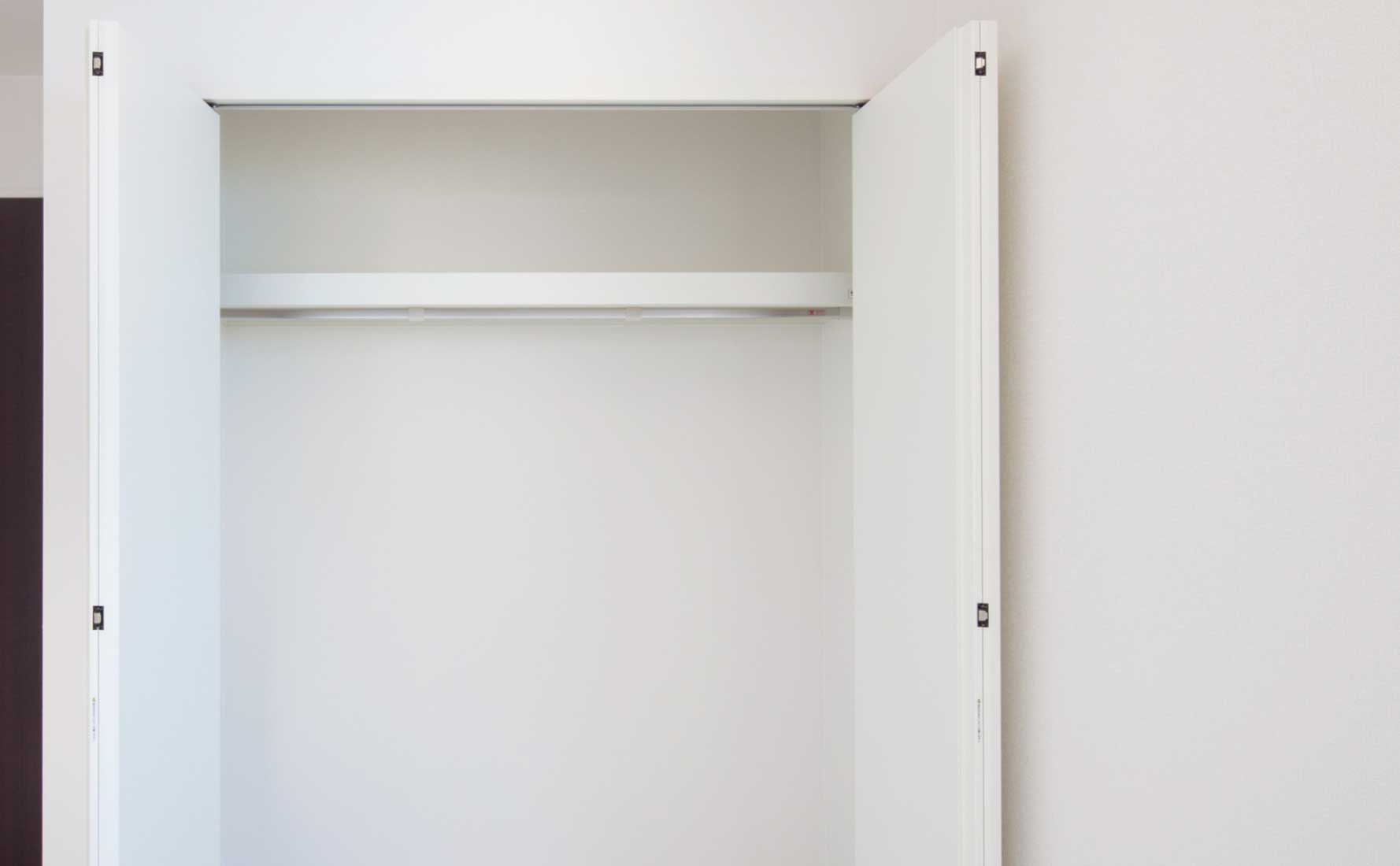 An empty white closet with open double doors and a single hanging rod inside.
